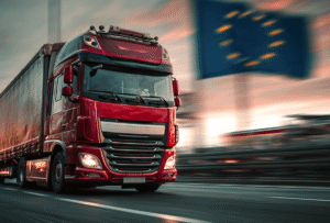 Pakiet Mobilności to największa od lat reforma transportu drogowego w Unii Europejskiej. Przepisy wprowadzane etapami od 2020 roku obejmują całe funkcjonowanie branży – od organizacji pracy kierowców po wymagania techniczne wobec pojazdów. Zmiany mają poprawić warunki pracy, wyrównać konkurencję między firmami transportowymi oraz zwiększyć bezpieczeństwo ruchu drogowego. Obejmują zarówno duże floty, jak i mniejszych przewoźników realizujących przewozy międzynarodowe. W tym artykule wyjaśniamy, czym jest unijny Pakiet Mobilności i jakie wprowadza zasady. Zawarliśmy w nim wszystkie najważniejsze wytyczne, które powinni znać przedsiębiorcy transportowi oraz kierowcy działający na terenie UE. Czym jest Pakiet Mobilności? Pakiet Mobilności to zestaw przepisów przyjętych w formie rozporządzeń Parlamentu Europejskiego, które regulują zasady wykonywania międzynarodowych przewozów drogowych na terenie UE. Ich celem jest ujednolicenie standardów, tak by firmy transportowe działały na równych zasadach, a kierowcy mieli zapewnione lepsze warunki pracy i odpoczynku. Pakiet obejmuje m.in.: przepisy dotyczące czasu jazdy i odpoczynku kierowców, zasady związane z delegowaniem kierowców i rozliczaniem ich płac, regulacje dotyczące dostępu do rynku, w tym przewozów kabotażowych i cross-trade, wymogi techniczne dotyczące wprowadzenia tachografów nowej generacji. W praktyce oznacza to, że wszystkie firmy transportowe – zarówno duże, jak i mniejsze – realizujące przewozy w krajach UE muszą dostosować swoje działania do nowych regulacji. Pakiet Mobilności stał się podstawowym punktem odniesienia dla branży transportowej w Europie oraz ważnym wyznacznikiem zasad wykonywania zawodu przewoźnika drogowego Cele pakietu mobilności Pakiet Mobilności nie powstał wyłącznie jako zbiór technicznych regulacji, ale jako odpowiedź na realne problemy branży transportowej działającej w ramach międzynarodowych przewozów drogowych na terenie UE. Zmiany wprowadzone przez rozporządzenia Parlamentu Europejskiego wynikają z potrzeby wyrównania warunków konkurencji i poprawy bezpieczeństwa w całej Unii. Dlatego główne cele pakietu to: poprawa warunków socjalnych kierowców – wprowadzenie przejrzystych zasad dotyczących czasu pracy i regularnych okresów odpoczynku, zapewnienie uczciwej konkurencji – ograniczenie zjawiska zaniżania kosztów poprzez obniżanie wynagrodzeń pracowników i ujednolicenie zasad rozliczania płac w różnych państwach członkowskich, zwiększenie bezpieczeństwa ruchu drogowego – dzięki rygorystycznej kontroli czasu jazdy i odpoczynków, co zmniejsza ryzyko wypadków spowodowanych przemęczeniem, harmonizacja przepisów – ujednolicenie prawa w całej UE, by uniknąć lokalnych rozbieżności, które dotąd utrudniały życie przewoźnikom realizującym przewozy międzynarodowe. W efekcie Pakiet Mobilności stał się nie tylko zbiorem norm prawnych, ale także narzędziem polityki społecznej i gospodarczej UE. Ma zapewniAć bardziej zrównoważony rozwój rynku i wyższe standardy pracy w całym sektorze transportu drogowego. Może zainteresuje Cię również: Cyfrowa spedycja 2025 – technologie w transporcie drogowym >>> Kogo dotyczy Pakiet Mobilności? Pakiet Mobilności obejmuje wszystkie podmioty wykonujące przewozy międzynarodowe na terenie Unii Europejskiej – zarówno duże floty ciężarowe, jak i mniejszych przewoźników działających z pomocą pojazdów o dopuszczalnej masie całkowitej min. 2,5 tony. Oznacza to, że nawet firmy transportowe wykorzystujące busy w transporcie towarów muszą dostosować się do nowych regulacji, choć część obowiązków wchodzi w życie etapami: od maja 2022 r. pojazdy 2,5–3,5 t w transporcie międzynarodowym objęto obowiązkiem posiadania licencji transportowej i zabezpieczenia finansowego, od lipca 2026 r. na te same pojazdy rozszerzone zostaną przepisy dotyczące tachografów i czasu pracy kierowców. Do grup objętych przepisami należą: kierowcy zawodowi wykonujący zadania służbowe w transporcie międzynarodowym, przedsiębiorcy transportowi, którzy muszą posiadać odpowiednią licencję transportową i spełniać wymogi dotyczące zabezpieczenia finansowego, firmy realizujące przewozy kabotażowe oraz cross trade, które podlegają szczegółowym zasadom delegowania, przewoźnicy działający w transporcie bilateralnym, dla których przewidziano częściowe wyłączenia z nowych regulacji. W praktyce Pakiet Mobilności dotyczy więc nie tylko największych przewoźników obsługujących transport na dużą skalę, ale każdego, kto świadczy usługi transportowe z pomocą pojazdów w obrębie Wspólnoty Europejskiej. To krok w stronę równego traktowania firm działających na rynku międzynarodowych przewozów drogowych. Zmiany dotyczące czasu pracy kierowców Pakiet Mobilności znacząco zmodyfikował zasady organizacji czasu pracy kierowców w transporcie międzynarodowym. Nowe przepisy mają chronić pracowników przed przemęczeniem, a jednocześnie zwiększyć przewidywalność i bezpieczeństwo w planowaniu tras. W centrum zmian znalazły się szczegółowe regulacje dotyczące tygodniowych odpoczynków. Nowe regulacje dotyczące tygodniowych okresów odpoczynku Najważniejsza zmiana to zakaz odbywania regularnych tygodniowych okresów odpoczynku (minimum 45 godzin) w kabinie pojazdu. Kierowca musi korzystać z hotelu lub innego miejsca z zapleczem noclegowym i sanitarnym, a koszt ponosi pracodawca. Regularne i skrócone odpoczynki tygodniowe – zasady Kierowca ma prawo w wyjątkowych sytuacjach odbyć dwa skrócone odpoczynki tygodniowe z rzędu (każdy trwający minimum 24 godziny zamiast 45). Taka możliwość istnieje tylko wtedy, gdy odpoczynki te przypadają poza krajem siedziby pracodawcy i poza miejscem zamieszkania kierowcy. W praktyce oznacza to, że kierowca może np. w pierwszym i drugim tygodniu wykonać odpoczynki po 24–30 godzin, a dopiero w kolejnym tygodniu musi odebrać pełny 45-godzinny odpoczynek wraz z rekompensatą za wcześniejsze skrócenia. W ciągu czterech kolejnych tygodni muszą się więc zmieścić co najmniej dwa regularne tygodniowe odpoczynki. Elastyczność czasu jazdy w wyjątkowych okolicznościach W wyjątkowych sytuacjach, gdy nie zagraża to bezpieczeństwu ruchu drogowego, a kierowca wraca do bazy firmy lub do swojego miejsca zamieszkania, może przedłużyć czas jazdy: o 1 godzinę – jeśli powrót dotyczy skróconego lub regularnego odpoczynku, o 2 godziny – jeśli wcześniej zrobił nieprzerwaną 30-minutową przerwę. Należy pamiętać, że takie przedłużenie czasu jazdy jest możliwe wyłącznie w drodze odstępstwa od zasad i stosowane jedynie w szczególnych, incydentalnych sytuacjach. Każde odstępstwo musi być udokumentowane w tachografie lub na wydruku, a wydłużony czas jazdy zrekompensowany odpoczynkiem trwającym co najmniej 9 godzin, wykorzystanym w ciągu maksymalnie trzech kolejnych tygodni. Zmiany dotyczące pracy nocnej i przerw Zgodnie z nowymi przepisami, w porze nocnej kierowca może pracować maksymalnie 10 godzin między dwoma odpoczynkami. Doprecyzowano również zasady dotyczące załóg: kierowca siedzący na fotelu pasażera może zaliczyć 45-minutową przerwę, o ile w tym czasie nie pomaga w prowadzeniu pojazdu. Przerwanie odpoczynku promem lub koleją Pakiet Mobilności dopuszcza możliwość przerwania dziennego odpoczynku lub skróconego tygodniowego odpoczynku, jeżeli kierowca odbywa przeprawę promową lub podróż koleją. Warunkiem jest, by kierowca miał do dyspozycji kabinę sypialną lub kuszetkę, co umożliwia mu odpoczynek w odpowiednich warunkach. Takie przerwanie jest dozwolone tylko w związku z wejściem lub zejściem z promu albo przy wsiadaniu i wysiadaniu z pociągu. Nie dotyczy jednak regularnych tygodniowych odpoczynków (45 godzin), które muszą być odbywane w hotelu lub innym miejscu z zapleczem noclegowym i sanitarnym, a ich koszt pokrywa pracodawca. Nowe przepisy dotyczące odpoczynków i czasu pracy mają chronić kierowców przed przemęczeniem i zwiększać bezpieczeństwo na drogach. Jednocześnie wymagają od firm lepszego planowania tras i pokrywania dodatkowych kosztów związanych z zakwaterowaniem poza pojazdem. Delegowanie kierowców i wynagrodzenia Unijny Pakiet Mobilności wprowadził przełomowe zmiany w zasadach delegowania kierowców i sposobie naliczania ich pensji. Kluczowe jest to, że podczas pracy w innym państwie kierowcy muszą otrzymywać wynagrodzenie zgodne z lokalnymi stawkami, co ma eliminować zjawisko dumpingu socjalnego. Co istotne, od sierpnia 2023 r. kierowca realizujący międzynarodowe przewozy drogowe nie jest już traktowany jako pracownik w podróży służbowej w rozumieniu Kodeksu pracy. Płaca minimalna i płaca zagraniczna w danym kraju Kierowcy wykonujący przewozy kabotażowe lub cross trade podlegają zasadom lokalnej płacy minimalnej. Oznacza to, że za czas pracy w danym kraju należy im się co najmniej taka sama stawka jak kierowcom miejscowym, a wysokość płacy minimalnej jest określana przez przepisy obowiązujące w danym państwie. Pracodawca nie może już zaliczać diet ani ryczałtów noclegowych jako części wynagrodzenia – są traktowane wyłącznie jako zwrot kosztów. Wyłączenia z delegowania – kiedy nie obowiązuje płaca lokalna? Nie wszystkie przewozy podlegają zasadom delegowania i obowiązkowi stosowania płacy minimalnej kraju, w którym kierowca aktualnie pracuje. Wyjątki te mają znaczenie praktyczne, ponieważ pozwalają przewoźnikom uniknąć dodatkowych kosztów w określonych sytuacjach. Do wyłączeń zaliczamy: Tranzyt – przejazd przez dane państwo bez załadunku ani rozładunku (np. przejazd z Polski do Hiszpanii przez Niemcy). Transport bilateralny – przewóz z kraju siedziby firmy do innego państwa UE lub powrót do kraju siedziby. Nawet jeśli kierowca wykona maksymalnie dwie dodatkowe operacje załadunku lub rozładunku w krajach tranzytowych po drodze, przewóz nadal jest traktowany jako bilateralny i nie podlega lokalnym stawkom płacy minimalnej. Te dwie operacje mogą odbywać się w tym samym kraju tranzytowym lub w dwóch różnych krajach tranzytowych. RODZAJ PRZEWOZU CZY OBOWIĄZUJE PŁACA MINIMALNA? UWAGI Tranzyt Nie Przejazd bez załadunku / rozładunku. Bilateralny Nie Dotyczy przewozów między krajem siedziby a innym państwem UE. Bilateralny + do 2 operacji Nie Dodatkowe 2 operacje możliwe w krajach tranzytowych po drodze lub przy powrocie. Kabotaż Tak Zawsze obowiązuje płaca lokalna. Cross trade Tak Zawsze obowiązuje płaca lokalna. System IMI – zgłaszanie delegowania kierowców Od lutego 2022 roku każdy przewoźnik musi zgłaszać delegowanie w systemie IMI (Internal Market Information). Kierowca powinien mieć przy sobie kopię zgłoszenia delegowania – może to być dokument elektroniczny z kodem QR, który ułatwia weryfikację podczas kontroli. Brak zgłoszenia grozi poważnymi karami finansowymi. Zmiany wprowadzone w Pakiecie Mobilności gwarantują większą przejrzystość zasad regulujących wynagrodzenie kierowców oraz lepszą ochronę przed zaniżaniem płac. Dzięki temu warunki pracy stają się bardziej przewidywalne, a kierowcy mogą liczyć na sprawiedliwe traktowanie niezależnie od kraju, w którym wykonują swoje obowiązki. Kabotaż, licencje transportowe i zabezpieczenie finansowe Pakiet Mobilności wprowadził bardziej restrykcyjne zasady dotyczące przewozów kabotażowych oraz wymogów związanych z licencjami transportowymi i zabezpieczeniami finansowymi. Zmiany te miały na celu ograniczenie nieuczciwej konkurencji i wyrównanie warunków działania przewoźników w różnych państwach członkowskich Unii Europejskiej. Nowe limity przewozów kabotażowych Kierowca może wykonać maksymalnie trzy operacje kabotażowe w ciągu siedmiu dni w jednym kraju. Po ich zakończeniu obowiązuje czterodniowa przerwa (cooling-off period), w trakcie której tym samym pojazdem nie wolno wykonywać kolejnych kabotaży w tym samym państwie. Rozwiązanie to zapobiega stałej obecności zagranicznych przewoźników na lokalnych rynkach i chroni transport krajowy przed nieuczciwą konkurencją cenową. Licencja transportowa i zabezpieczenie finansowe Od maja 2022 roku obowiązek posiadania licencji transportowej oraz spełniania wymogów dotyczących zabezpieczenia finansowego został rozszerzony także na mniejsze firmy transportowe korzystające w transporcie międzynarodowym na terenie UE z pojazdów o DMC od 2,5 do 3,5 tony. Wymagane zabezpieczenie wynosi 1800 euro na pierwszy pojazd i 900 euro na każdy kolejny. Nowe regulacje sprawiły, że dostęp do rynku międzynarodowych przewozów drogowych jest bardziej przejrzysty i oparty na jednolitych zasadach. Jednocześnie oznacza to dla przewoźników konieczność lepszego planowania działalności oraz poniesienia dodatkowych kosztów. Nowe limity przewozów kabotażowych Kierowca może wykonać maksymalnie trzy operacje kabotażowe w ciągu siedmiu dni w jednym kraju. Po ich zakończeniu obowiązuje czterodniowa przerwa (cooling-off period), w trakcie której tym samym pojazdem nie wolno wykonywać kolejnych kabotaży w tym samym państwie. Nowy przepis zapobiega stałej obecności zagranicznych przewoźników na rynkach lokalnych. Dzięki temu rynek transportu krajowego w poszczególnych państwach jest lepiej chroniony przed nieuczciwą konkurencją cenową. Licencja transportowa i zabezpieczenie finansowe Od maja 2022 roku nawet mniejsze firmy transportowe korzystające z busów w transporcie międzynarodowym muszą posiadać licencję transportową oraz spełniać wymogi dotyczące zabezpieczenia finansowego – 1800 euro na pierwszy pojazd i 900 euro na każdy kolejny. Warto podkreślić, że obowiązek ten dotyczy wyłącznie przewozów międzynarodowych. Wprowadzone wymogi w zakresie kabotażu i licencji uporządkowały zasady dostępu do rynku, eliminując przewoźników działających w sposób nieuczciwy lub bez odpowiedniego zabezpieczenia finansowego. Dzięki temu rynek transportu międzynarodowego stał się bardziej przewidywalny i stabilny, co sprzyja firmom działającym zgodnie z prawem. Tachografy i nowe wymagania techniczne Pakiet Mobilności nakłada obowiązek korzystania z nowoczesnych urządzeń rejestrujących – inteligentnych tachografów drugiej generacji (G2V2). To jedno z najważniejszych narzędzi w kontroli przestrzegania czasu pracy i zasad delegowania. Właśnie w tym obszarze wprowadzono jedne z najbardziej istotnych zmian w pakiecie mobilności, które stopniowo obejmują wszystkie pojazdy realizujące przewozy międzynarodowe drogowe na terenie UE. Inteligentne tachografy drugiej generacji – czym się różnią? Nowe tachografy G2V2 wprowadzają szereg usprawnień względem starszych modeli. Automatycznie rejestrują przekraczanie granic z wykorzystaniem GNSS, zapisując dodatkowe punkty lokalizacyjne w trasie. Kierowcy mogą wprowadzać dane o załadunku i rozładunku, a służby kontrolne zyskują możliwość zdalnego odczytu informacji bez zatrzymywania pojazdu. Urządzenia mają większą pamięć, lepsze zabezpieczenia przed manipulacją, opcję zdalnej aktualizacji oprogramowania oraz dodatkowe funkcje raportowania. Dzięki temu tachografy drugiej generacji zwiększają przejrzystość rozliczeń, ułatwiają zarządzanie flotą i ograniczają ryzyko naruszeń przepisów. Obowiązkowa wymiana tachografów analogowych i cyfrowych Pakiet przewiduje obowiązek stosowania nowych urządzeń w pojazdach wykonujących przewozy międzynarodowe. Zmiany wprowadzane są etapami: od 20 sierpnia 2023 r. – wszystkie nowo rejestrowane pojazdy muszą być wyposażone w tachografy G2V2, do 31 grudnia 2024 r. – wymiana tachografów analogowych i starszych cyfrowych (G1) w pojazdach wykonujących przewozy międzynarodowe, 1 stycznia – 28 lutego 2025 r. – okres przejściowy, w którym kierowcy byli pouczani i edukowani w zakresie konieczności wymiany, bez nakładania mandatów, do 20 sierpnia 2025 r. – wymiana tachografów inteligentnych pierwszej generacji (G2V1), od 1 lipca 2026 r. – obowiązek montażu G2V2 w pojazdach o dopuszczalnej masie całkowitej 2,5–3,5 t wykonujących przewozy międzynarodowe. Warto podkreślić, że w starszych pojazdach wykorzystywanych wyłącznie w transporcie krajowym nadal można korzystać z tachografów analogowych i cyfrowych pierwszej generacji (G1), o ile pojazdy te nie wyjeżdżają poza granice kraju. Nowe funkcjonalności i rozszerzone kontrole Od 2025 roku kierowcy muszą okazać dane z tachografu z ostatnich 56 dni (wcześniej 28). Do czasu pełnego wdrożenia G2V2 nadal wymagane są manualne wpisy kraju po przekroczeniu granicy – na pierwszym bezpiecznym postoju. Dzięki nowym tachografom kontrola w transporcie stała się bardziej szczegółowa, a jednocześnie mniej uciążliwa, bo część weryfikacji odbywa się zdalnie. Dla firm transportowych oznacza to konieczność inwestycji w sprzęt, ale także większą pewność, że działają zgodnie z obowiązującymi przepisami. Nowe tachografy to nie tylko wymóg prawny – to także narzędzie, które ułatwia kontrolę czasu pracy kierowców, monitorowanie przewozów, a także poprawia przejrzystość rozliczeń związanych z delegowaniem kierowców w różnych państwach członkowskich UE. Przeczytaj też: Tachograf – kiedy wymienić, by uniknąć mandatu w UE? >>> Powrót kierowcy i pojazdu – jak zmieniły się przepisy? Jednym z najbardziej dyskutowanych tematów w ramach Pakietu Mobilności jest obowiązek organizacji powrotów kierowców do miejsca zamieszkania lub bazy firmy oraz zasady dotyczące powrotów pojazdów do kraju siedziby przedsiębiorstwa. Zmiany te mają zapewnić, by kierowcy nie spędzali wielu tygodni w trasie bez kontaktu z domem, a przedsiębiorstwa faktycznie prowadziły działalność w kraju rejestracji. Obowiązkowy powrót kierowcy do swojego miejsca zamieszkania lub bazy Każdy kierowca wykonujący zadania służbowe w transporcie międzynarodowym musi mieć możliwość powrotu do swojego miejsca zamieszkania albo do bazy firmy co najmniej raz na cztery tygodnie. W tym czasie powinien wykorzystać regularne tygodniowe okresy odpoczynku. Obowiązek ten spoczywa na pracodawcy, który organizuje pracę w taki sposób, by umożliwić kierowcy powrót. Wszystkie koszty związane z zakwaterowaniem poza kabiną oraz samym powrotem pokrywa firma. Co więcej, przedsiębiorca musi prowadzić dokumentację potwierdzającą spełnienie tego wymogu i przechowywać ją w siedzibie, tak by mogła zostać okazana podczas ewentualnej kontroli. Powrót pojazdu co 8 tygodni – zmiana po wyroku Trybunału Sprawiedliwości UE Przepisy początkowo wymagały, by pojazd wracał do kraju siedziby raz na 8 tygodni. Rozwiązanie to było jednak krytykowane m.in. za zwiększanie liczby pustych przebiegów i sprzeczność z celami Europejskiego Zielonego Ładu. W efekcie w 2024 roku Trybunał Sprawiedliwości UE unieważnił ten obowiązek. Obecnie pojazdy nie muszą już wracać co 8 tygodni, ale przewoźnicy nadal są zobowiązani do prowadzenia rzeczywistej i stałej działalności w kraju rejestracji. Oznacza to konieczność posiadania bazy eksploatacyjnej z odpowiednią liczbą miejsc postojowych, faktyczne zarządzanie flotą z poziomu państwa siedziby oraz dbanie o dobrą reputację firmy. Długotrwały brak powrotów pojazdów do kraju może być traktowany przez organy kontrolne jako przesłanka wskazująca na brak takiej działalności. Co to oznacza w praktyce? Nowe regulacje wymagają starannego planowania tras i grafików, by kierowca mógł nie tylko dostarczyć ładunek do miejsca docelowego, ale także regularnie wracać do domu. To ważny element dbałości o standardy pracy, bezpieczeństwo na drogach oraz przejrzystość działania firm transportowych w całej Unii Europejskiej. Kary i sankcje w ramach Pakietu Mobilności Przepisy wprowadzone w ramach Pakietu Mobilności są rygorystycznie egzekwowane, a ich naruszenie wiąże się z wysokimi sankcjami zarówno dla kierowców, jak i dla przedsiębiorców transportowych. Celem systemu kar jest nie tylko dyscyplinowanie uczestników rynku, ale także zapewnienie uczciwej konkurencji i zwiększenie bezpieczeństwa ruchu drogowego w całej Unii Europejskiej. Kary dla kierowców Kierowcy muszą przestrzegać zasad dotyczących czasu jazdy, odpoczynków oraz prawidłowej obsługi tachografów. Naruszenia, takie jak brak wpisu kraju po przekroczeniu granicy, odbywanie regularnego odpoczynku w kabinie czy przekraczanie dopuszczalnego czasu jazdy, mogą skutkować mandatami sięgającymi nawet kilku tysięcy euro – w zależności od kraju i stopnia przewinienia. Kary dla przedsiębiorców transportowych Firmy transportowe odpowiadają m.in. za posiadanie wymaganych licencji, prawidłowe zgłoszenie delegowania kierowców czy rozliczanie wynagrodzeń zgodnie z lokalną płacą minimalną. Naruszenia w tych obszarach wiążą się z karami, które w poszczególnych państwach mogą wynosić od kilku do nawet kilkudziesięciu tysięcy euro. Najpoważniejsze przewinienia, jak manipulowanie tachografami czy uporczywe łamanie przepisów, grożą utratą dobrej reputacji i cofnięciem licencji transportowej. System kar i sankcji w ramach pakietu mobilności został skonstruowany tak, by zmusić całą branżę transportową do przestrzegania obowiązujących przepisów. Surowe konsekwencje mają wyeliminować zjawisko dumpingu socjalnego, poprawić warunki pracy kierowców i zwiększyć bezpieczeństwo ruchu drogowego w całej Unii Europejskiej. Podsumowanie Pakiet Mobilności to największa w ostatnich latach zmiana w europejskim transporcie drogowym, która wpływa zarówno na czas pracy kierowców, jak i na zasady działania firm transportowych. Nowe regulacje obejmują m.in. regularne tygodniowe okresy odpoczynku, obowiązek cyklicznego powrotu kierowcy do swojego miejsca zamieszkania, zasady dotyczące delegowania kierowców oraz obowiązek wymiany tachografów na inteligentne urządzenia drugiej generacji. Choć wdrożenie przepisów wiąże się z kosztami i nowymi obowiązkami, ich celem jest poprawa warunków pracy, zapewnienie uczciwej konkurencji i zwiększenie bezpieczeństwa ruchu drogowego na terenie całej Unii Europejskiej. Dla tych, którzy szybko się dostosują, Pakiet Mobilności może stać się szansą na wzmocnienie pozycji w branży transportowej i budowanie przewagi konkurencyjnej w przyszłości. Najczęściej zadawane pytania (FAQ) Czy Pakiet Mobilności jeszcze obowiązuje? Tak, Pakiet Mobilności obowiązuje i jego przepisy są wdrażane etapami aż do 2026 roku. Ostatnie zmiany dotyczą głównie wymiany tachografów i obowiązków firm w ramach przewozów międzynarodowych realizowanych w Unii Europejskiej. Co daje Pakiet Mobilności? Pakiet ma zapewniać lepsze warunki pracy kierowców wykonujących przewozy międzynarodowe na terenie Unii Europejskiej i wyrównane zasady konkurencji dla firm transportowych. Dzięki podniesieniu standardów dotyczących czasu pracy kierowców przyczynia się do zwiększenia bezpieczeństwa ruchu drogowego. Ile zarabia kierowca w Pakiecie Mobilności? Zgodnie z Pakietem Mobilności, kierowca otrzymuje wynagrodzenie co najmniej na poziomie płacy minimalnej obowiązującej w danym kraju, w którym wykonuje pracę. W praktyce jego pensja często jest wyższa, ponieważ uwzględnia również dodatki, staż pracy czy warunki określone przez pracodawcę. Do kiedy należy wymienić tachografy analogowe wg Pakietu Mobilności? Tachografy analogowe należało wymienić do 31 grudnia 2024 roku w pojazdach wykonujących międzynarodowe przewozy drogowe na terenie Unii Europejskiej. Od 1 stycznia 2025 r. wszystkie takie pojazdy muszą być wyposażone w inteligentne tachografy drugiej generacji (G2V2). Brak wymiany jest traktowany jako poważne naruszenie i wiąże się z ryzykiem wysokich kar podczas kontroli.